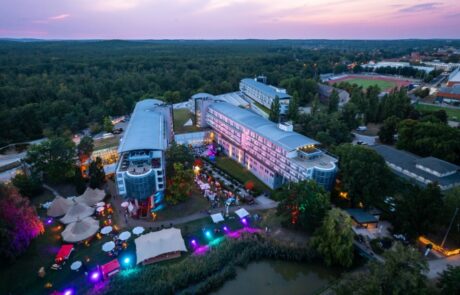 Das Kongresshotel Potsdam am Abend aus der Luft betrachtet. Der Eventgarten ist ein belebter Ort mit viel Licht, verschiedenen Ständen und Zelten. 